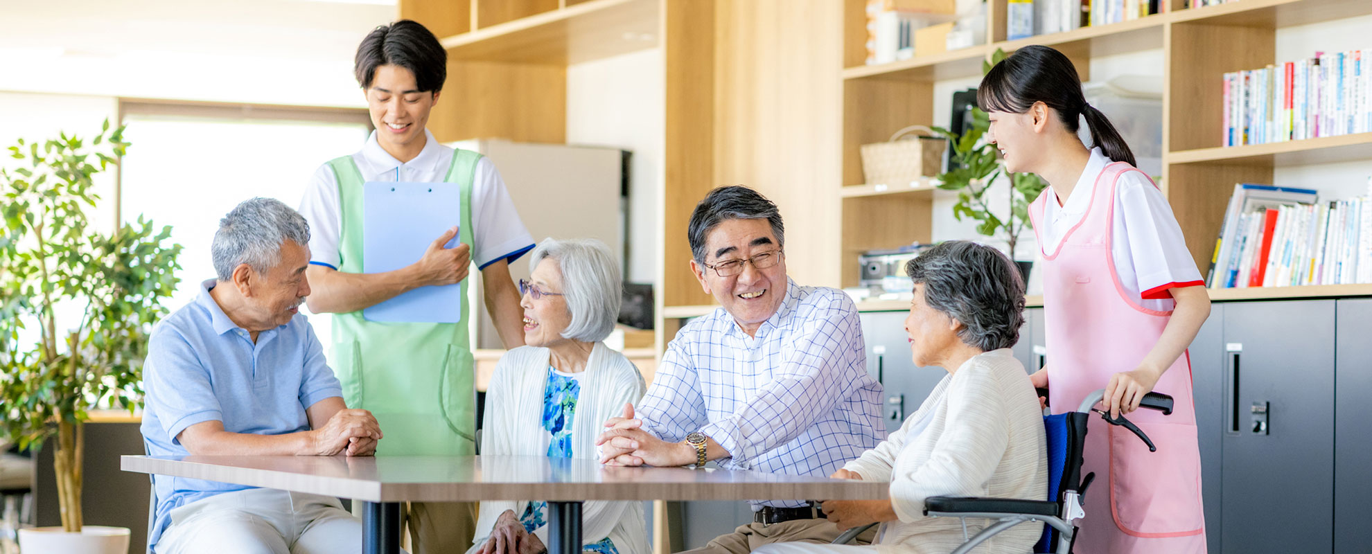 イスに座り談笑する高齢者と立って会話している介護士